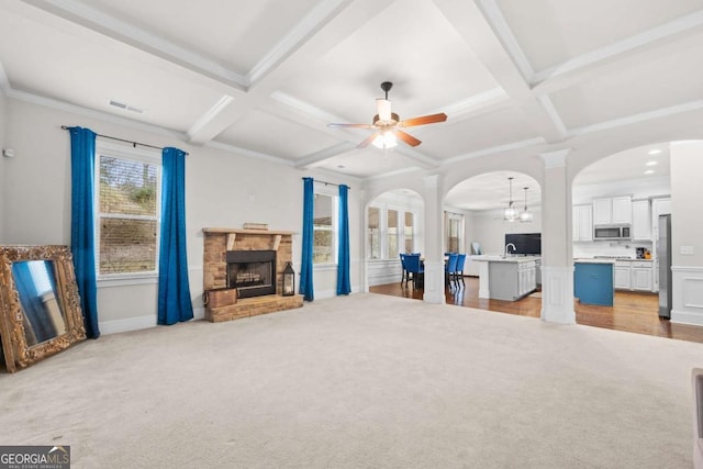 living room with coffered ceiling, a stone fireplace, and light colored carpet