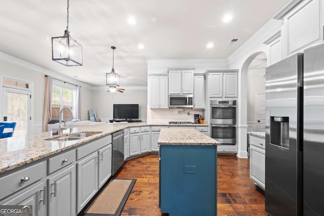 kitchen featuring sink, appliances with stainless steel finishes, hanging light fixtures, a center island, and ornamental molding