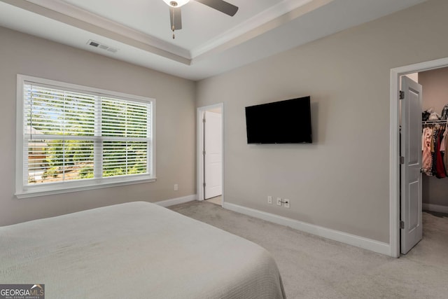 carpeted bedroom featuring a raised ceiling, a walk in closet, ceiling fan, and a closet