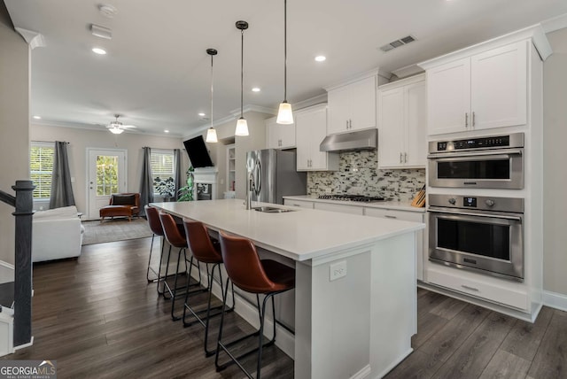 kitchen featuring hanging light fixtures, white cabinetry, appliances with stainless steel finishes, and a center island with sink