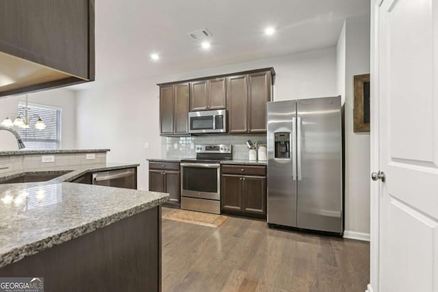 kitchen with dark brown cabinetry, sink, light stone counters, appliances with stainless steel finishes, and backsplash