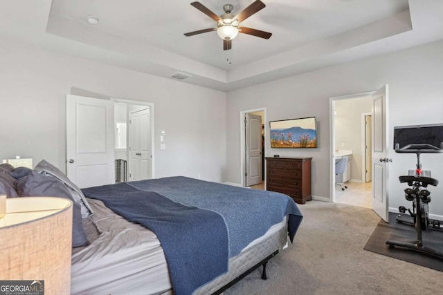 bedroom with ceiling fan, light colored carpet, a raised ceiling, and ensuite bath