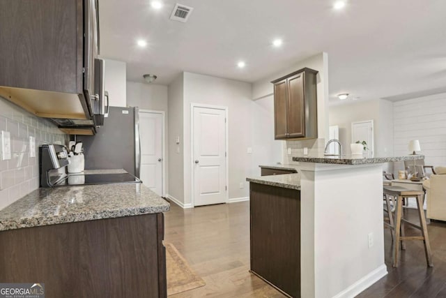 kitchen featuring stone counters, range, a kitchen bar, dark hardwood / wood-style flooring, and kitchen peninsula