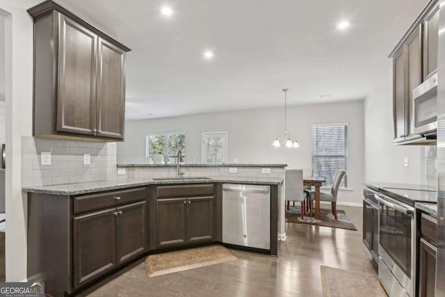 kitchen with sink, stainless steel appliances, light stone counters, decorative backsplash, and kitchen peninsula