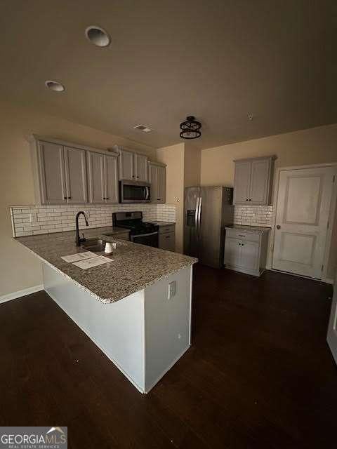 kitchen featuring sink, tasteful backsplash, dark hardwood / wood-style flooring, kitchen peninsula, and stainless steel appliances