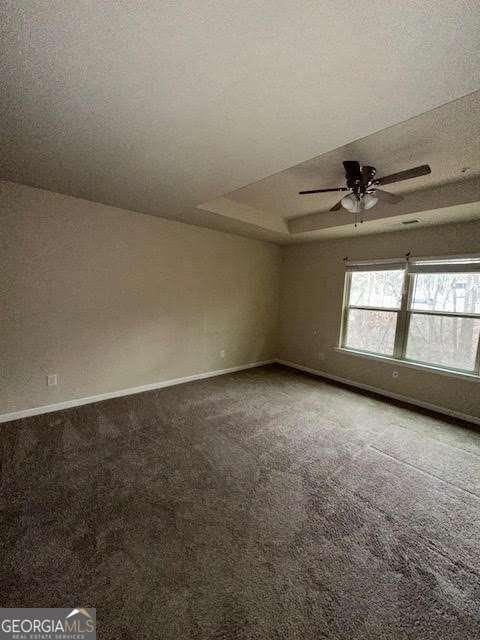 unfurnished room with ceiling fan, carpet flooring, a tray ceiling, and a textured ceiling