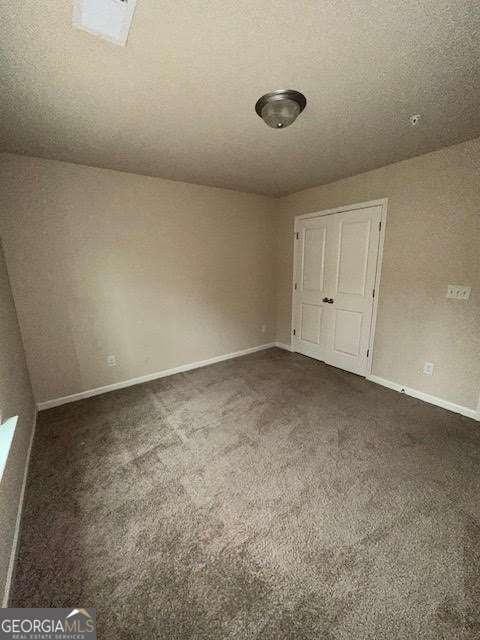 interior space with dark colored carpet, a textured ceiling, and a closet