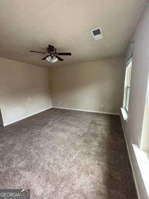 unfurnished room featuring ceiling fan, a textured ceiling, and dark colored carpet