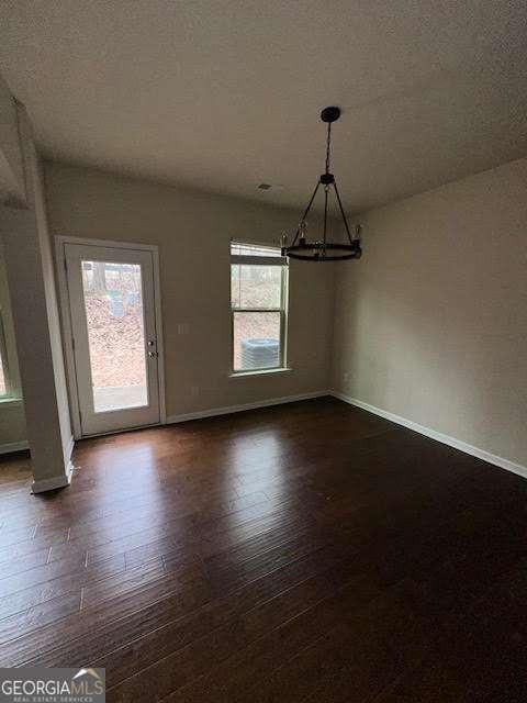 unfurnished dining area with a notable chandelier, a textured ceiling, and dark hardwood / wood-style flooring