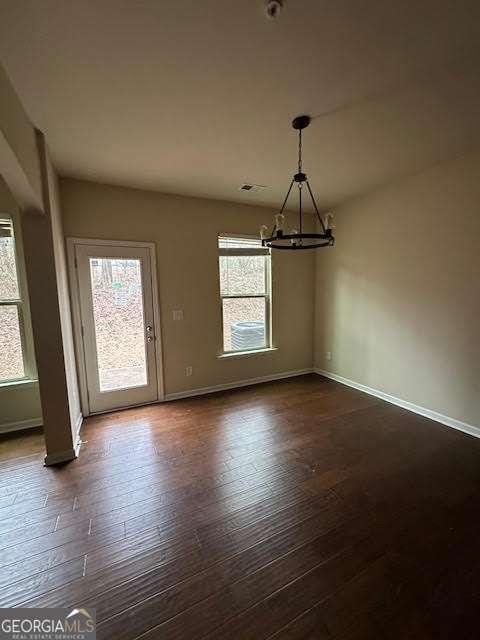 unfurnished dining area featuring a notable chandelier, dark hardwood / wood-style floors, and a healthy amount of sunlight