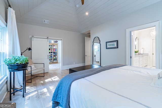 bedroom featuring light hardwood / wood-style flooring, high vaulted ceiling, and a barn door