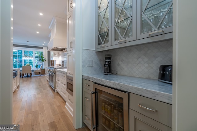 kitchen featuring decorative light fixtures, wine cooler, light hardwood / wood-style floors, stainless steel appliances, and light stone countertops