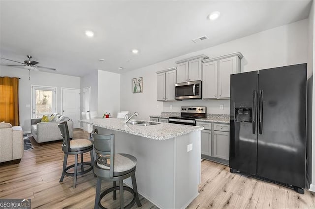 kitchen featuring sink, appliances with stainless steel finishes, gray cabinetry, light hardwood / wood-style floors, and a center island with sink