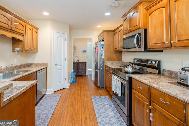 kitchen with sink, a textured ceiling, light wood-type flooring, stainless steel appliances, and light stone countertops