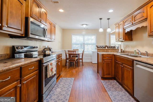 kitchen featuring dark wood-type flooring, sink, hanging light fixtures, a textured ceiling, and appliances with stainless steel finishes