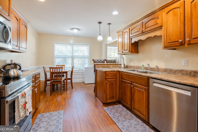 kitchen with sink, light wood-type flooring, appliances with stainless steel finishes, kitchen peninsula, and pendant lighting