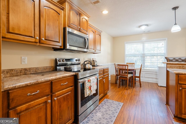 kitchen featuring decorative light fixtures, light wood-type flooring, a textured ceiling, and appliances with stainless steel finishes