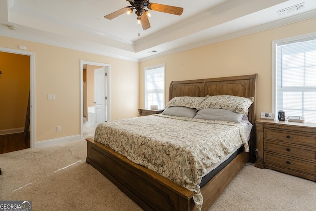 bedroom featuring a raised ceiling, ensuite bathroom, light carpet, and multiple windows