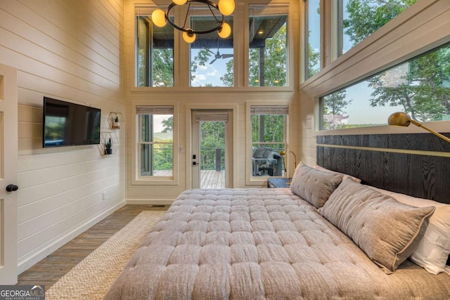 bedroom with multiple windows, access to exterior, wood-type flooring, and wood walls