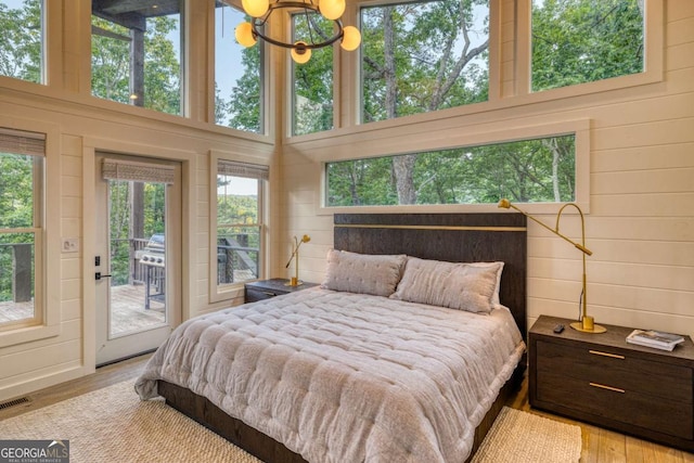 bedroom with light wood-type flooring, access to outside, wooden walls, and a towering ceiling