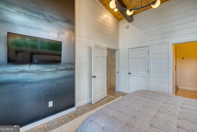 bedroom featuring wooden walls, light wood-type flooring, ceiling fan, wood ceiling, and beam ceiling