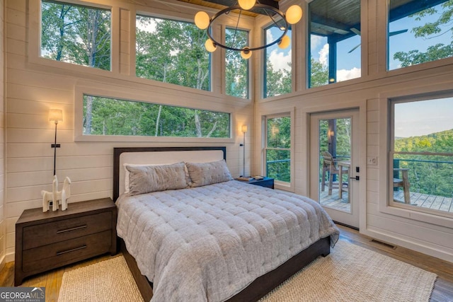 bedroom featuring multiple windows, a high ceiling, access to outside, and light wood-type flooring