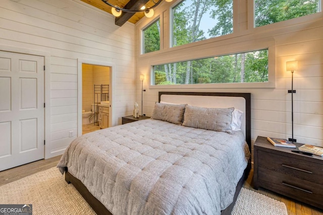 bedroom featuring a high ceiling, ensuite bathroom, wooden walls, and light hardwood / wood-style floors