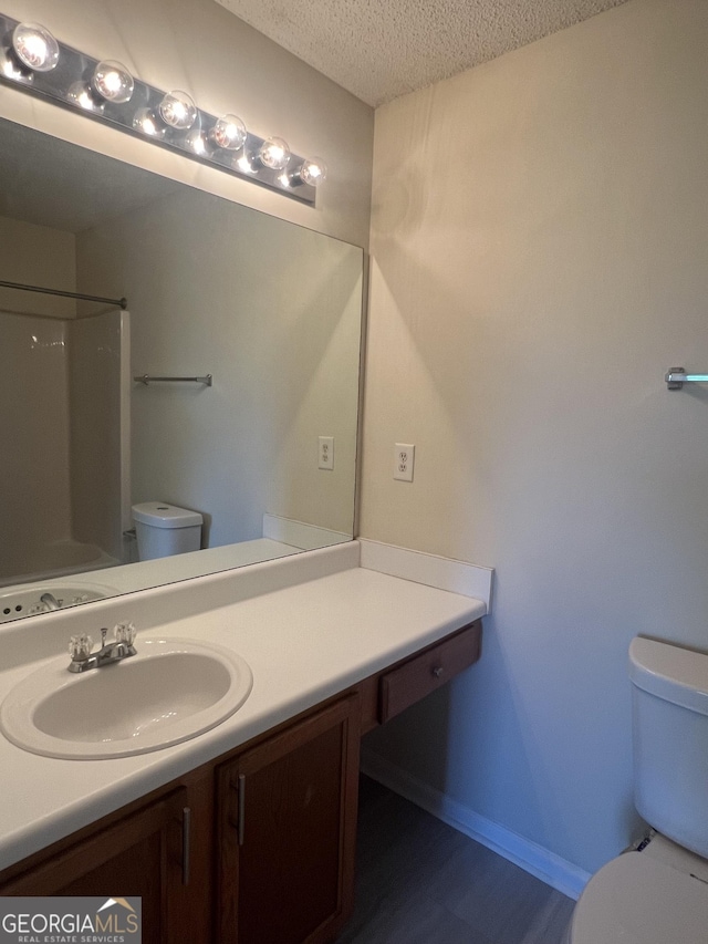 bathroom with vanity, toilet, a textured ceiling, and walk in shower