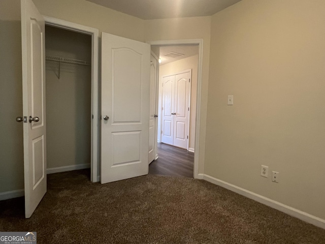 unfurnished bedroom with dark colored carpet and a closet