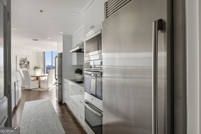 kitchen with appliances with stainless steel finishes, dark wood-style flooring, light countertops, under cabinet range hood, and white cabinetry