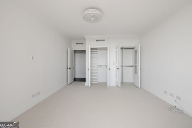 unfurnished bedroom with light carpet, visible vents, ornamental molding, and multiple closets