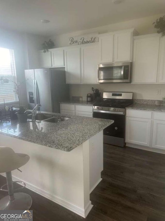 kitchen featuring a breakfast bar, white cabinetry, sink, light stone counters, and stainless steel appliances