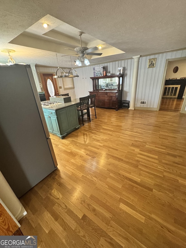 kitchen with stainless steel refrigerator, decorative light fixtures, light hardwood / wood-style floors, a tray ceiling, and a textured ceiling