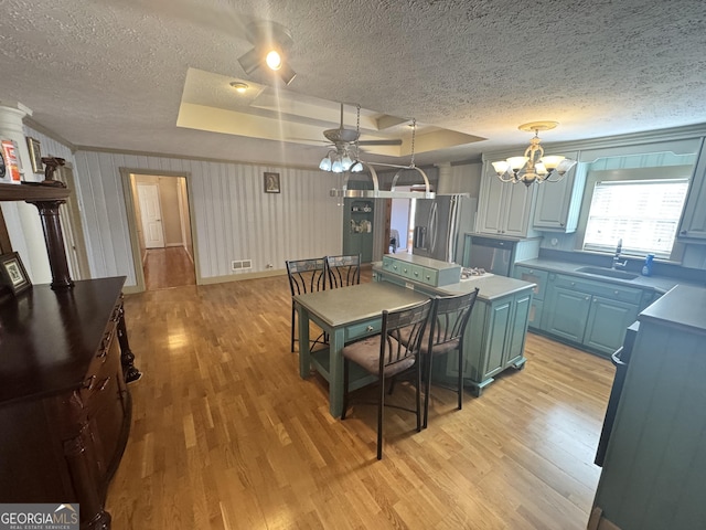 kitchen with pendant lighting, sink, stainless steel fridge, light hardwood / wood-style flooring, and a raised ceiling