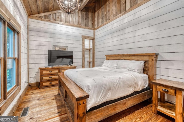 bedroom with hardwood / wood-style flooring, lofted ceiling, wooden walls, and an inviting chandelier