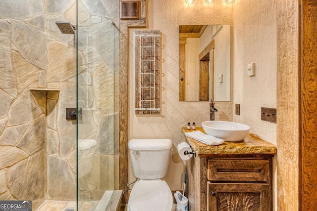 bathroom featuring a tile shower, vanity, and toilet