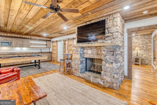 living room featuring light hardwood / wood-style flooring, wooden ceiling, a barn door, and ceiling fan