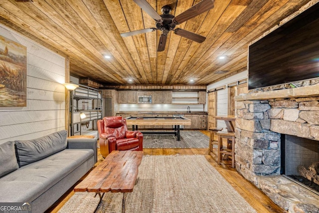 living room with a stone fireplace, sink, wooden ceiling, a barn door, and light hardwood / wood-style floors