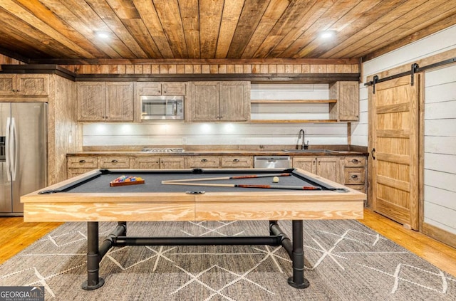 recreation room featuring wooden walls, sink, wood ceiling, a barn door, and light wood-type flooring