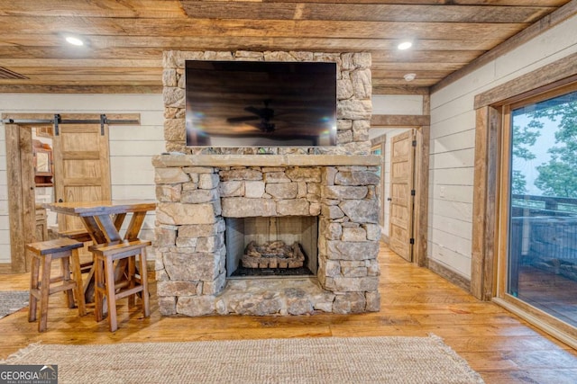 interior details with wood-type flooring, a stone fireplace, wooden ceiling, a barn door, and wood walls