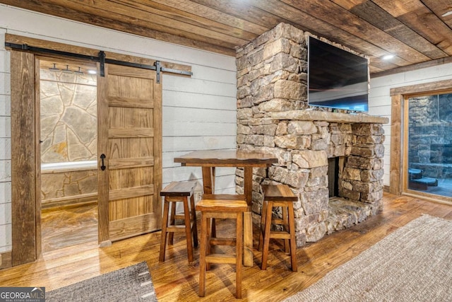 dining space with hardwood / wood-style floors, a fireplace, wood walls, a barn door, and wooden ceiling