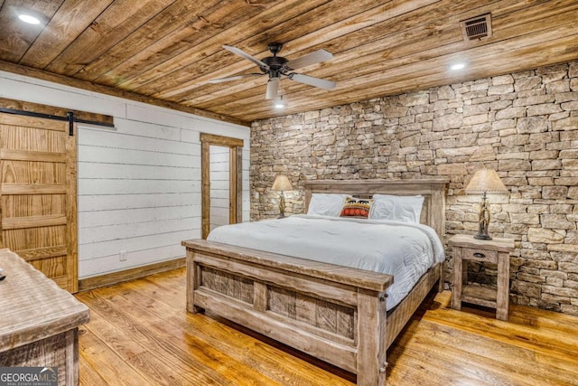 bedroom with wood ceiling, a barn door, and light hardwood / wood-style floors