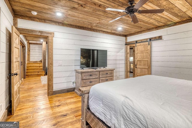 bedroom with wooden walls, a barn door, light wood-type flooring, and wooden ceiling