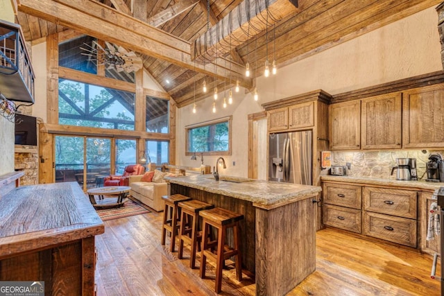 kitchen with light hardwood / wood-style floors, high vaulted ceiling, an island with sink, and stainless steel refrigerator with ice dispenser