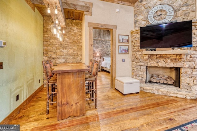 bar featuring wood counters, a fireplace, beam ceiling, and light hardwood / wood-style flooring