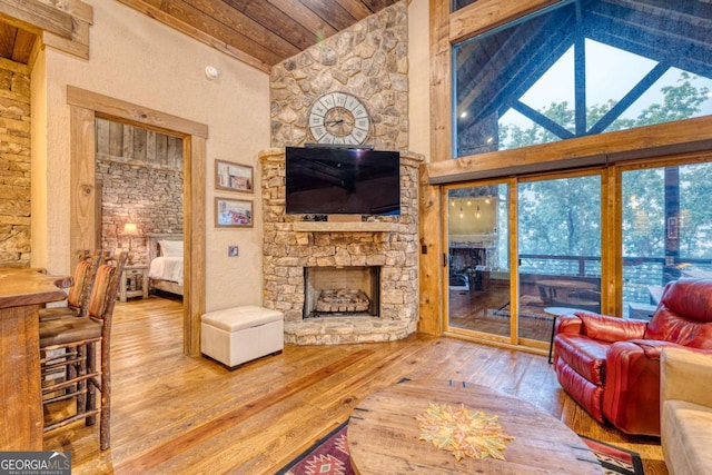 living room featuring hardwood / wood-style flooring, a stone fireplace, high vaulted ceiling, and wooden ceiling