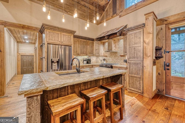 kitchen featuring stainless steel refrigerator with ice dispenser, sink, range, an island with sink, and a high ceiling