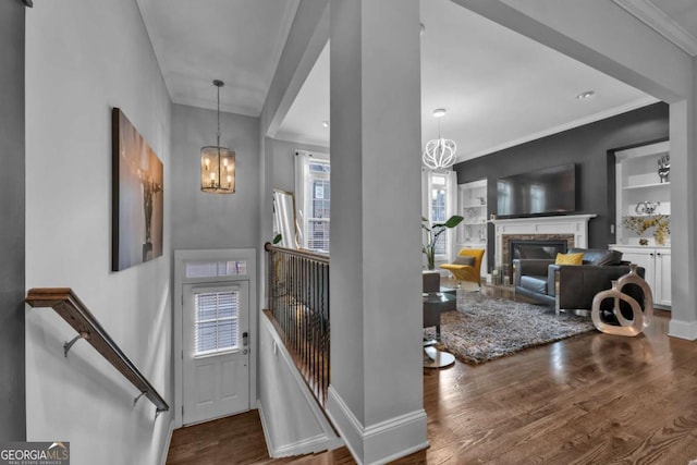 foyer featuring wood-type flooring, a stone fireplace, ornamental molding, and a chandelier