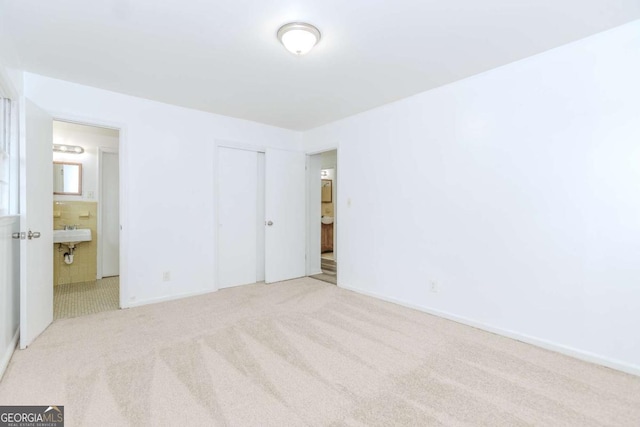 unfurnished bedroom featuring sink, ensuite bath, light colored carpet, and a closet