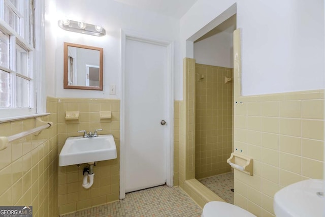 bathroom with toilet, sink, tile walls, a tile shower, and tile patterned flooring